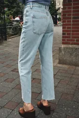 Pantalón de jean color crudo, de tiro alto, corte recto y largo tobillero. Tiene cinco bolsillos, cierre frontal con cremallera y botón metálico.