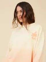 Sweater color crema con degradé a naranja, con cuello redondo y logo estampado de palmera en el pecho.