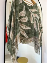 Blusa verde con estampado de hojas beige, cuello redondo y corte asimétrico.
