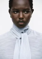 Blusa de manga larga color celeste claro con textura sutil, cuello alto con lazo largo incorporado que cae al frente.