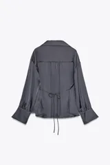 Camisa gris de satén con cuello solapa, escote en pico, mangas largas abullonadas y cierre frontal con botones metálicos.