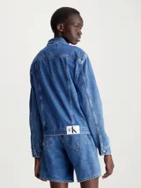 Campera de jean azul medio de corte clásico, con cuello en punta, bolsillos de parche en el pecho, bolsillos de hendidura en la cintura, botones metálicos de la marca y logo de Calvin Klein en el bolsillo del pecho.