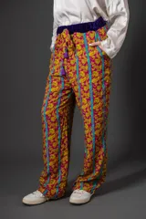 Pantalón de viscosa con estampado floral en tonos fucsia y amarillo, con rayas verticales turquesas. Presenta cintura elastizada con detalle de terciopelo violeta y lazo con borlas.