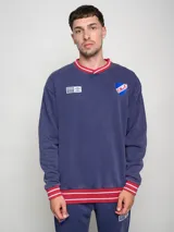 Buzo azul marino de felpa con efecto lavado, cuello en V y puños en color rojo con rayas blancas. Presenta el escudo del Club Nacional de Football y el logo de Umbro bordados en el pecho.
