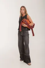 Bolso de hombro tipo hobo de cuero gamuzado color camel, con correa ancha ajustable con hebilla metálica plateada. La correa presenta un estampado de vaca (cow print) en tonos blanco y marrón.