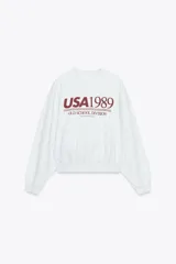 Sudadera gris de cuello redondo y manga larga con puños y cintura acanalados. Estampa frontal con texto "USA1989 OLD SCHOOL DIVISION" en color bordó.