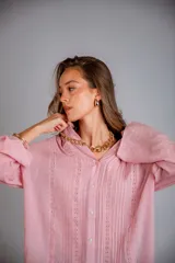 Camisa color beige claro, de corte holgado, con cuello clásico, cierre frontal con botones, mangas largas con puños abotonados y detalles de broderie en la parte delantera.