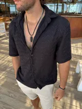 Camisa negra tejida de manga corta con cuello camisero y cierre frontal con botones.