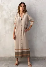 Vestido tejido de punto color beige, largo midi, con cuello polo y botones frontales. Posee mangas cortas y detalles de franjas horizontales en tonos marrones y naranjas en puños y ruedo.