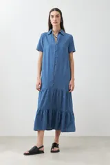 Maxi vestido camisero de jean azul con cuello clásico, manga corta, cierre frontal con botones y falda amplia con volantes.