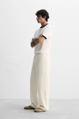 Pantalón color crema de corte amplio, con cintura elástica ajustable con cordón, bolsillos laterales y trasero, cierre frontal con cremallera y botón.