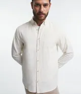 Camisa de hombre de corte regular, color borgoña, confeccionada en tela Oxford con efecto jaspeado. Tiene cuello inglés, abotonadura frontal, mangas largas con puños abotonados y bolsillo de parche en el pecho.