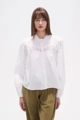 Camisa blanca de algodón con mangas largas abullonadas y cuello mao con volado. Presenta un canesú con detalles de encaje calado en el frente.