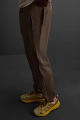Pantalón deportivo color marrón oscuro, corte regular fit, confeccionado en tejido técnico ligero y elástico. Cuenta con cintura elástica ajustable con cordón, bolsillos frontales con cierre de cremallera, bolsillo trasero con cierre de cremallera oculta en costura y bajo ajustable con elástico.
