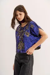 Camisa azul con lentejuelas y bordados dorados con cuello redondo y mangas cortas con aberturas.
