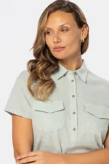 Camisa de lino color verde claro, de manga corta, con cuello clásico, cierre frontal con botones y dos bolsillos con solapa en el pecho.