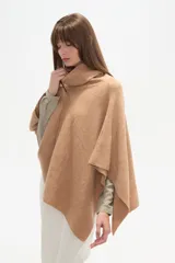 Poncho tejido color tostado, con cuello alto tipo tortuga y diseño asimétrico en el ruedo.