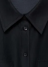 Camisa negra de lyocell y poliéster, con cuello camisero, dos bolsillos de solapa en el pecho, manga larga con puños abotonados y cierre frontal con botones. Diseño recto y cierre de lazo ajustable.