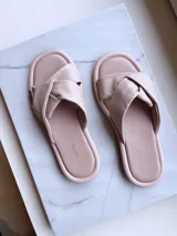 Sandalias bajas color rosa nude, sin talón, confeccionadas en cuero, con tira ancha sobre el empeine con detalle de nudo.