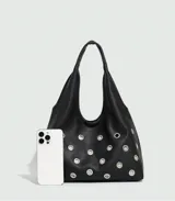 Bolso tipo hobo de cuero sintético negro con apliques de ojales metálicos plateados.