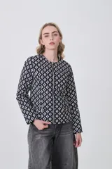 Chaqueta de manga larga con cuello a la base y cierre frontal. Presenta un estampado geométrico repetitivo en blanco y negro.