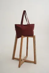 Bolso grande color bordo de material suave, con asas largas para llevar al hombro.