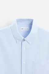 Camisa azul marino de corte regular fit, confeccionada en tejido de algodón Oxford. Tiene cuello abotonado, manga larga con puños abotonados, bolsillo de parche en el pecho y cierre frontal con botones.