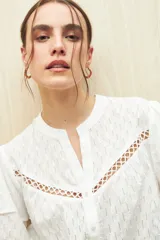 Camisa blanca de algodón liviano con diseño calado, cuello mao, mangas cortas abullonadas y detalle de pasamanería en el frente.
