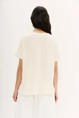 Remera color crudo de viscosa y poliéster, con moldería holgada, hombros caídos y mangas rebatidas. Presenta bordados de motivos egipcios en hilo de colores.