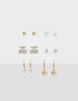 Set de seis pares de aros dorados con diferentes diseños: bolitas, cerezas con strass, strass solitarios, perlas colgantes y corazones colgantes.