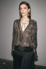 Camisa de viscosa con estampado paisley en blanco y negro. Cuello redondo con escote pico ajustable con cordones, mangas largas con elástico y volantes en los puños, bajo asimétrico y cierre frontal con botones forrados.