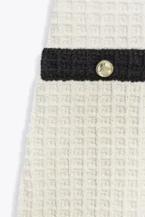 Vestido corto color crema confeccionado en tejido elástico con textura. Tiene escote redondo, tirantes anchos y falsos bolsillos de vivo con botón dorado en el delantero.