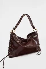 Bolso de hombro marrón oscuro con acabado brillante, asa trenzada y ojales metálicos en los laterales.