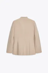Blazer color beige, sin solapa, de manga larga con bolsillos de vivo en el delantero y cierre frontal con gancho metálico.