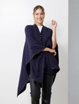 Ruana blanca de tejido suave, con ribete de eco cuero negro en los bordes y cierre frontal con botones metálicos dorados.