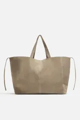 Bolso tipo shopper color topo, fabricado en piel con acabado serraje. Cuenta con dos asas de mano y un bolsillo pequeño con cierre mediante cremallera en su interior.