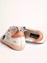 Zapatillas urbanas Golden Goose modelo Super-Star, de cuero blanco con detalles en marrón y estrella negra con glitter en el lateral. Diseño con efecto desgastado en la suela y cordones.
