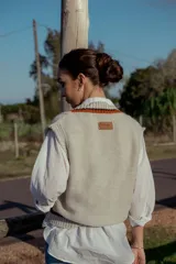 Chaleco tejido color crema con cuello en V y ribetes en naranja y negro. Diseño sin mangas y corte holgado. Ideal para usar sobre camisas o remeras de manga larga.