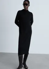 Vestido midi negro de tejido de punto fino, con cuello alto y manga larga. Diseño recto y terminaciones en canalé.