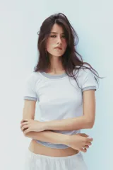 Camiseta blanca de corte slim fit, cuello redondo y manga corta con acabados en puntilla. Tiene detalle de frunces en los laterales y tejido combinado a contraste efecto doble en cuello, mangas y ruedo.