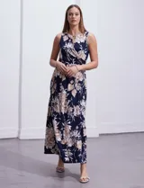 Vestido largo de seda fría con estampado floral en tonos beige y blanco sobre fondo azul marino. Tiene cuello redondo cruzado con abertura y aplique metálico.