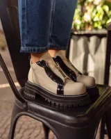 Botines de cuero negro con paneles laterales de charol, cierre frontal con cremallera y suela track.