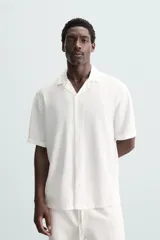 Camisa de calce relajado confeccionada en tejido fluido de mezcla de viscosa, color blanco. Presenta cuello bowling, manga corta, aberturas laterales en el bajo y cierre frontal con botones al tono.