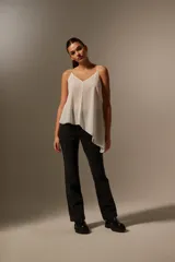Blusa blanca de poliéster con breteles finos, escote en V, corte asimétrico y volados.