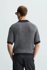 Polo de hombre de corte relajado, tejido de punto de algodón a rayas verticales en tonos gris y negro. Tiene cuello solapa, cierre frontal con botones y mangas cortas.