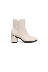 Botín de cuero liso color blanco hueso, de caña corta y punta redondeada. Posee un tacón ancho y bajo, y una suela negra gruesa.