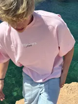 Remera rosa de corte recto con estampado en la espalda que incluye el texto "Itta Tours", "Tour", y nombres de ciudades como Ibiza, Madrid, Andorra, Barcelona y Formentera.