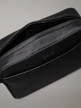 Bolso bandolera negro de Calvin Klein, confeccionado en piel sintética suave. Tiene correa ancha ajustable, cierre de cremallera, bolsillo exterior y bolsillo interior.