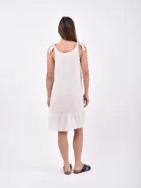 Vestido corto color crudo, de lino, con breteles finos con lazos y volado en el ruedo.