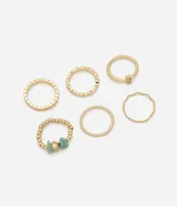 Set de seis anillos dorados con diferentes diseños: uno con textura, uno con lunares y pedrería, uno con strass, uno con cuentas y piedras turquesas, uno con forma ondulada y uno liso.